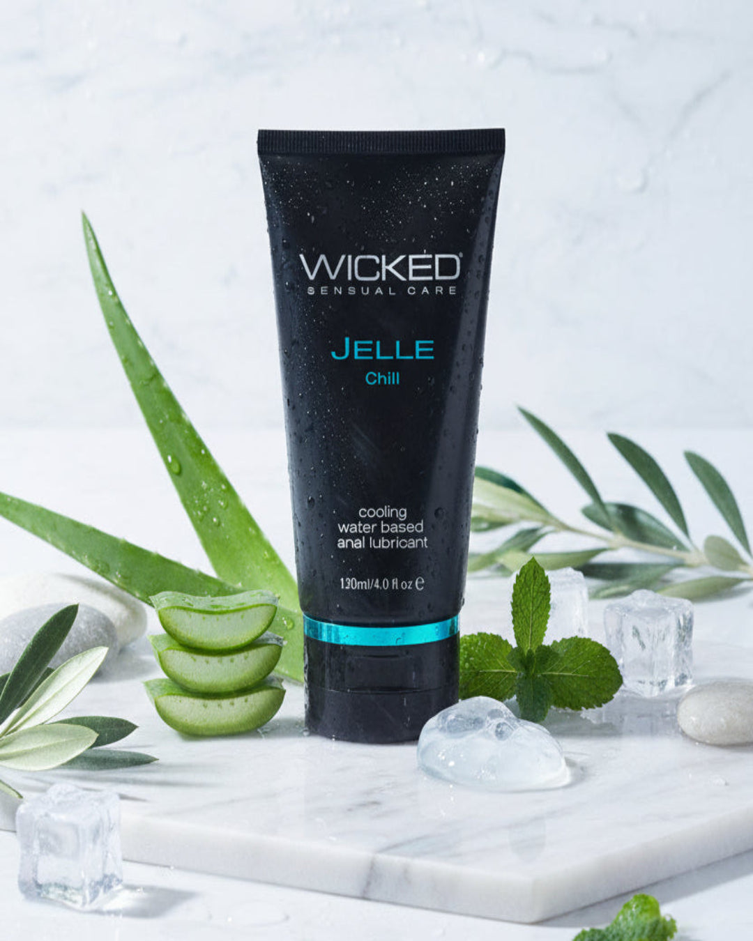 A tube of Wicked Anal Jelle Cooling Water Based Anal Lube with Aloe sits on a marble surface, surrounded by aloe vera, mint leaves, and ice cubes—all glistening with water droplets.