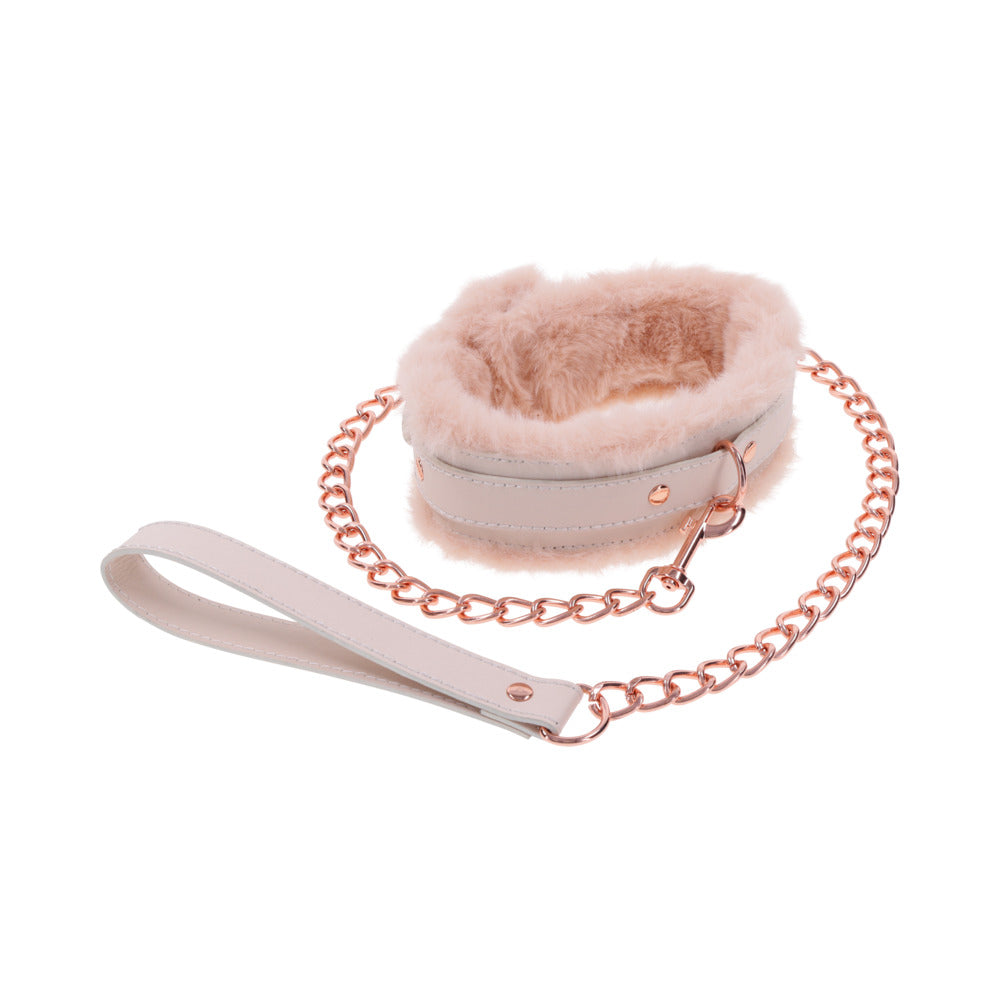 The Peaches 'n Cream Fur Collar and Leash by Sportsheets features a pair of pink faux fur-lined wrist cuffs connected by a rose gold chain with a matching leather strap, ideal for crafting intimate moments and exploring gentle bondage.