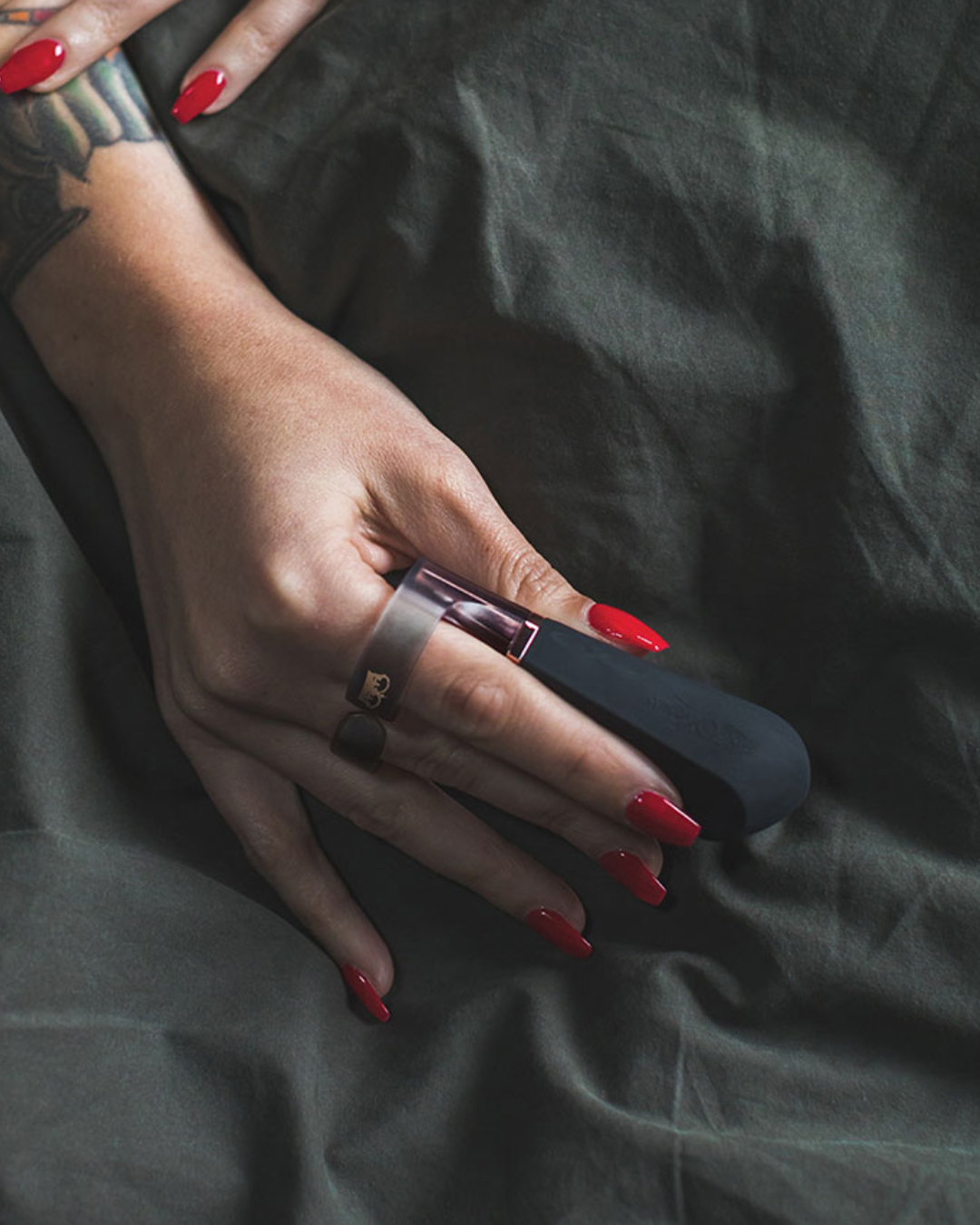 Hot Octopuss Digit Silicone Rechargeable Finger Vibrator held by a woman with long nails on a black silk sheet