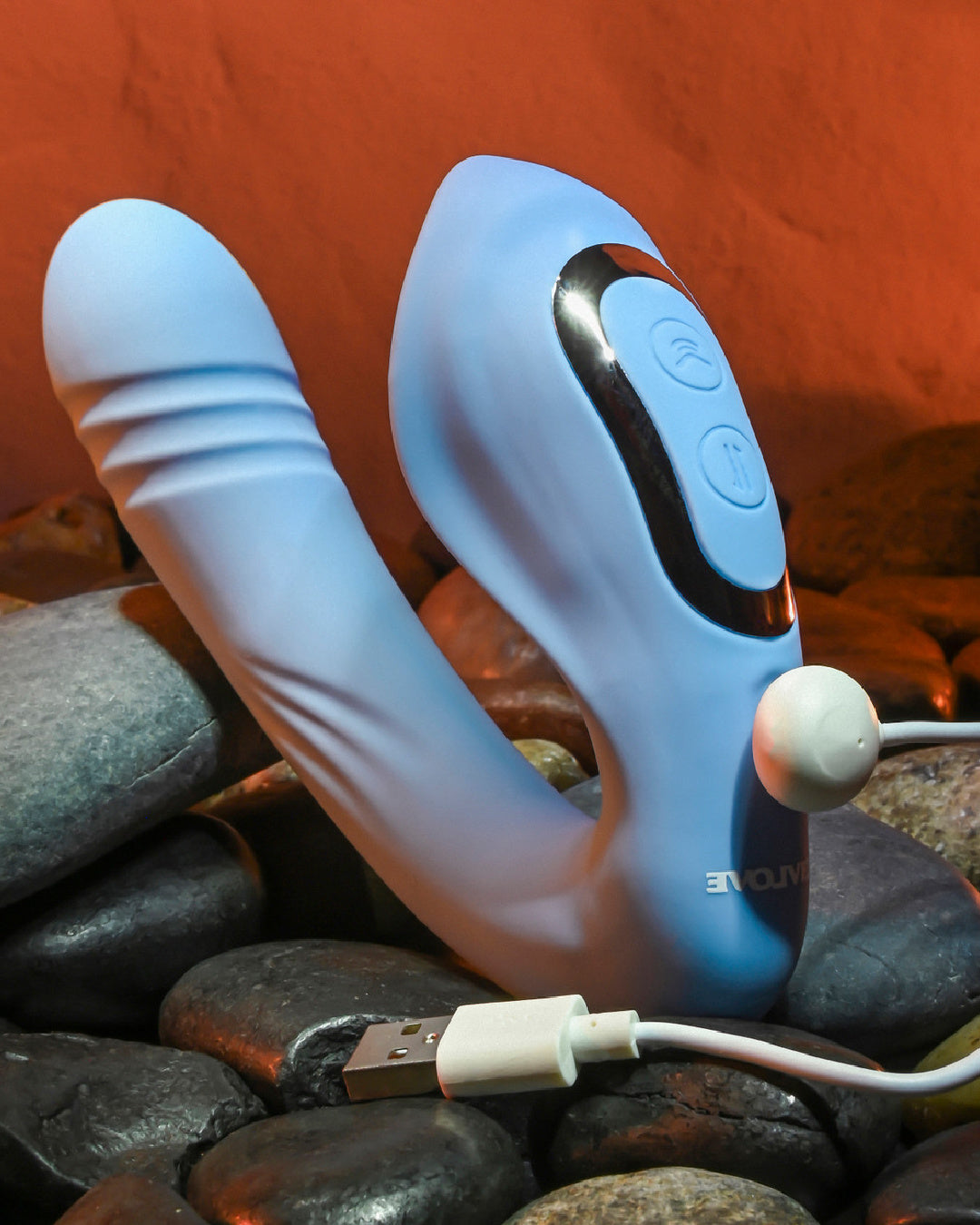 Tap and Thrust Dual Stimulation Thrusting Vibrator sitting on rocks with charger cable plugged in