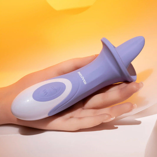 A hand holds a purple and white personal massager, the Lix & Kisses Swirling Tongue Oral Sex Vibrator by Evolved Novelties, made from phthalate-free silicone against a warm orange background. The device features a curved, ergonomic design with control buttons on the handle.