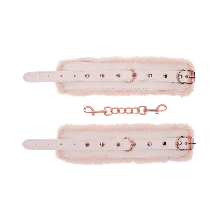 The Peaches 'n Cream Fur Handcuffs by Sportsheets are beige and fluffy, featuring adjustable straps and rose gold-tone buckles. These luxurious faux fur handcuffs are connected by a detachable chain, offering an elegant addition to your bondage accessories collection.