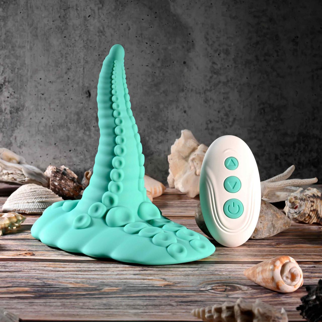 The Octopus Tentacle Insertable Remote Controlled Grinder in turquoise and its white remote are displayed on a wooden surface among seashells, set against a textured gray background.