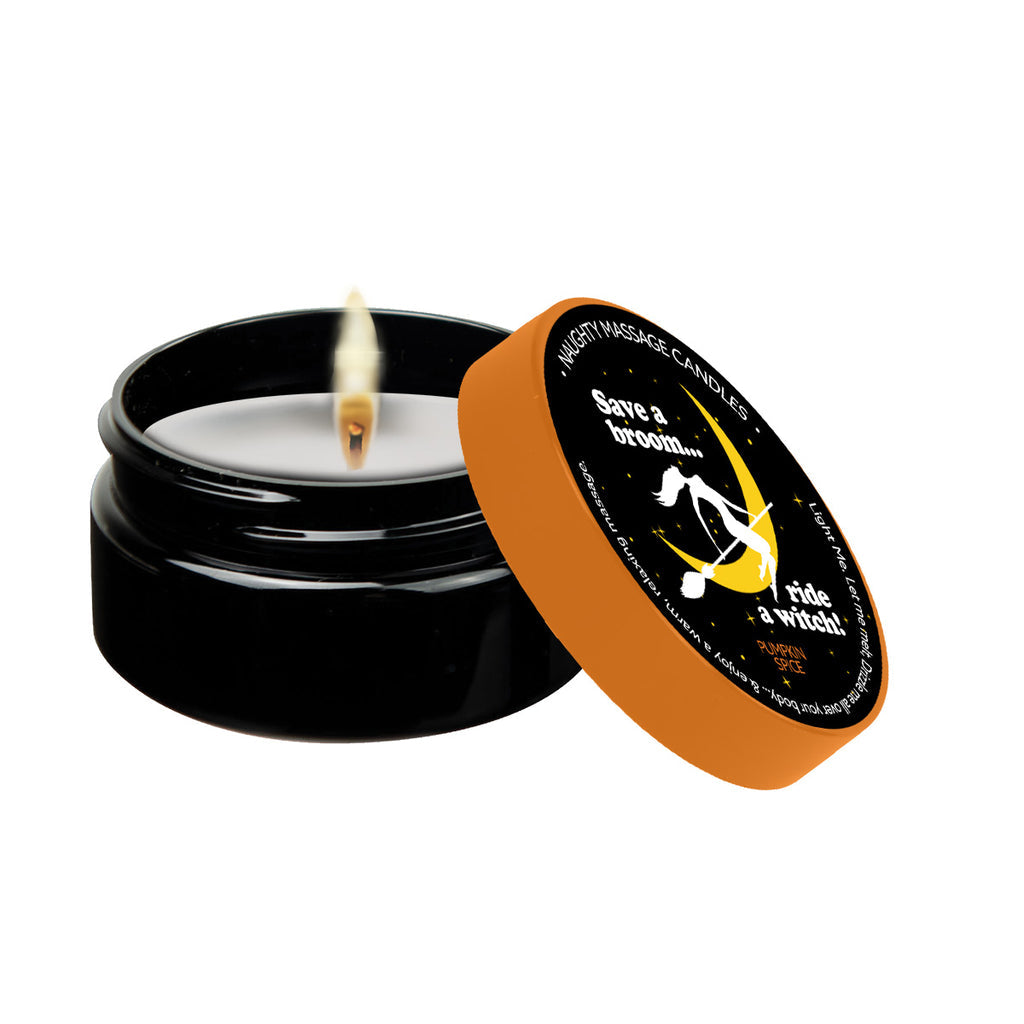 A lit Kama Sutra Pumpkin Spice Erotic Massage Candle, with its black container and orange lid set to the side. The lid showcases a design of a witch riding a broomstick along with the text, "Save a Broom... Ride a Witch!