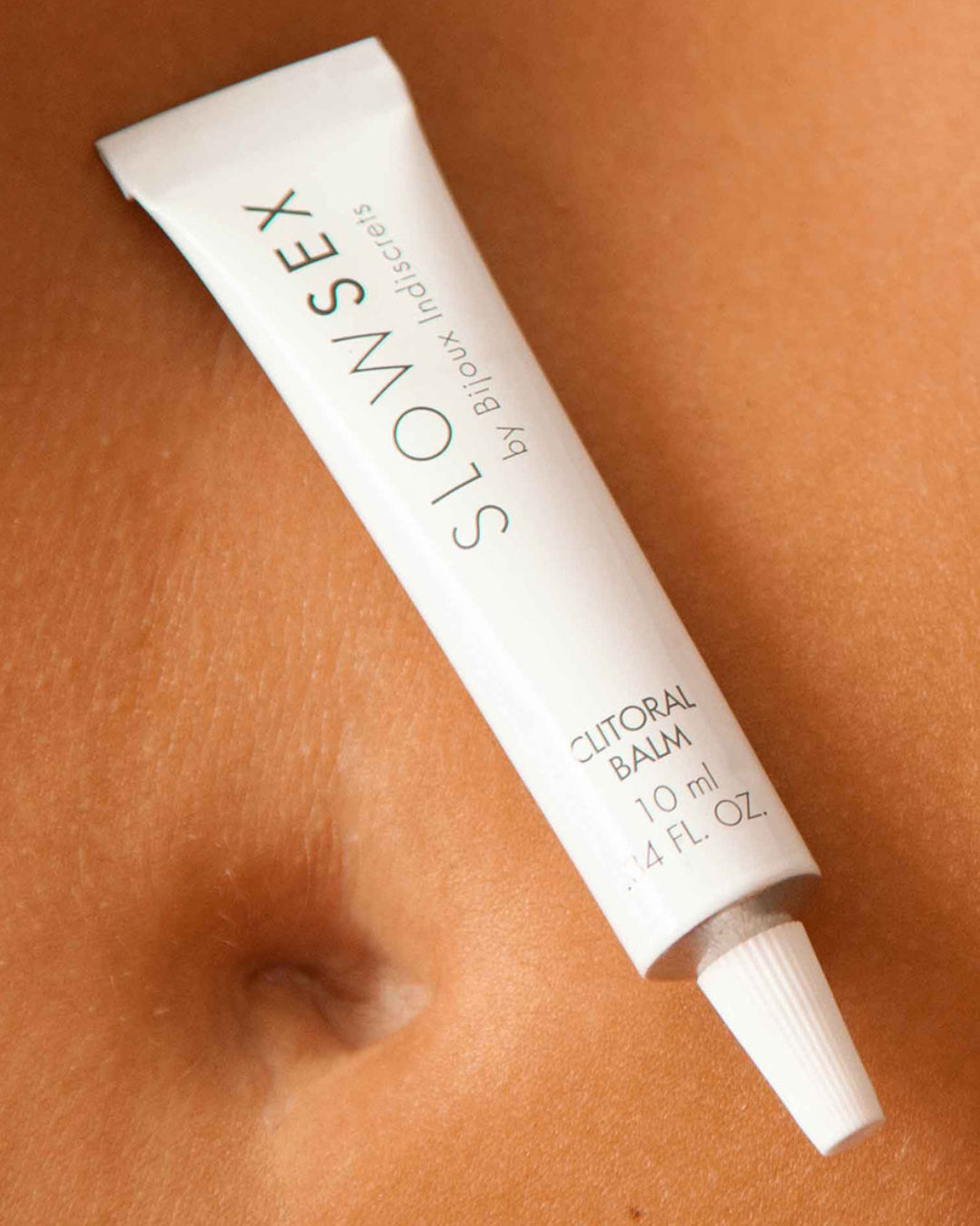 Bijoux Indiscrets Slow Sex Clitoral Balm tube on mode's stomach